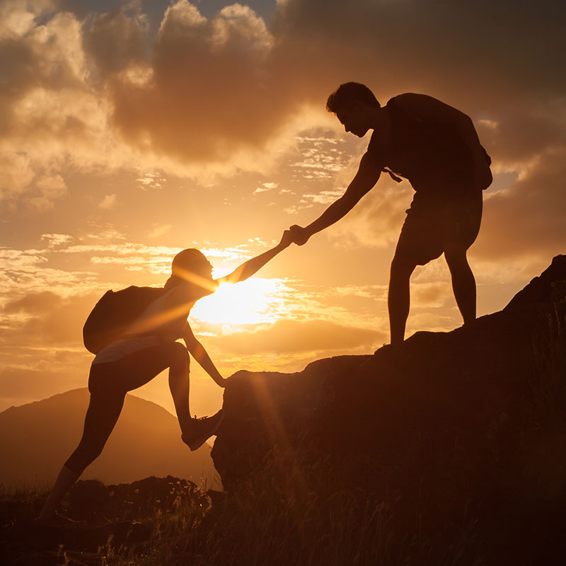 Hiker helping another hiker up a mountain at sunset