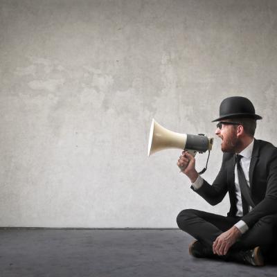 Man wearing top hat sitting on the ground speaking into a megaphone