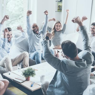 Team members sitting around a table celebrating with hands in the air