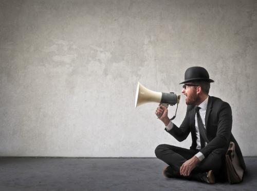 Man wearing top hat sitting on the ground speaking into a megaphone