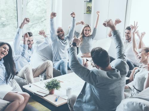 Team members sitting around a table celebrating with hands in the air