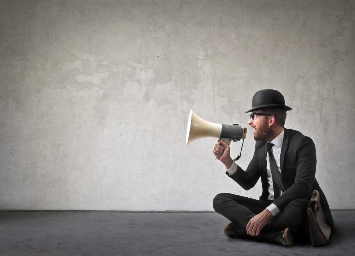 Man wearing top hat sitting on the ground speaking into a megaphone