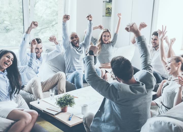 Team members sitting around a table celebrating with hands in the air